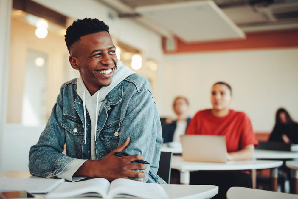 Male student sitting in university classroom looking away and smiling.
