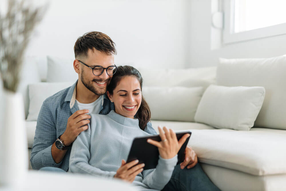 Two lovers, sitting on the sofa, watching something online.