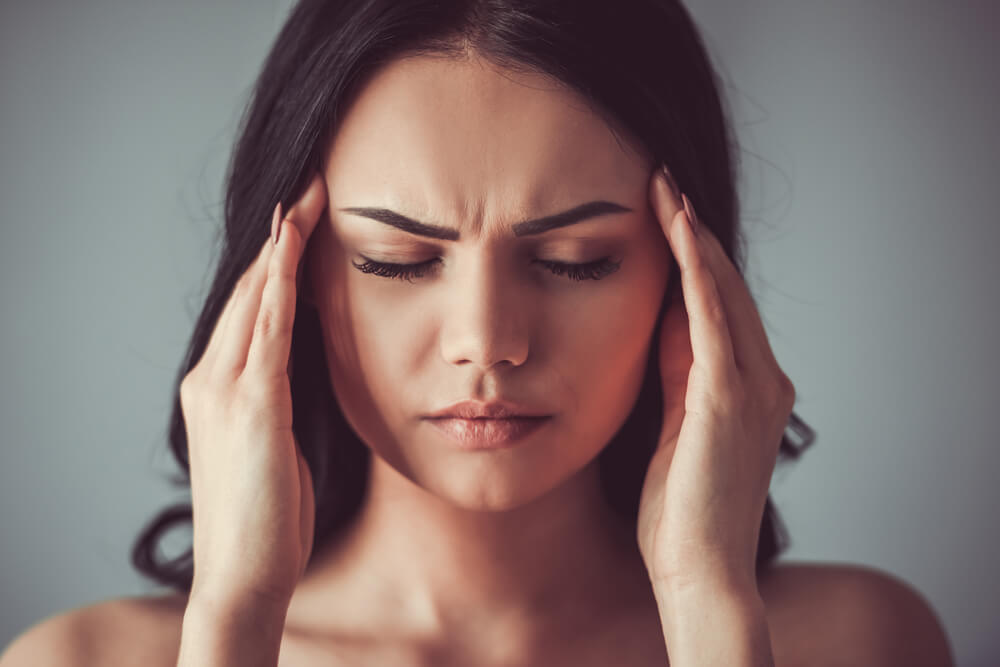 Portrait of beautiful young brunette with bare shoulders touching her temples feeling stress