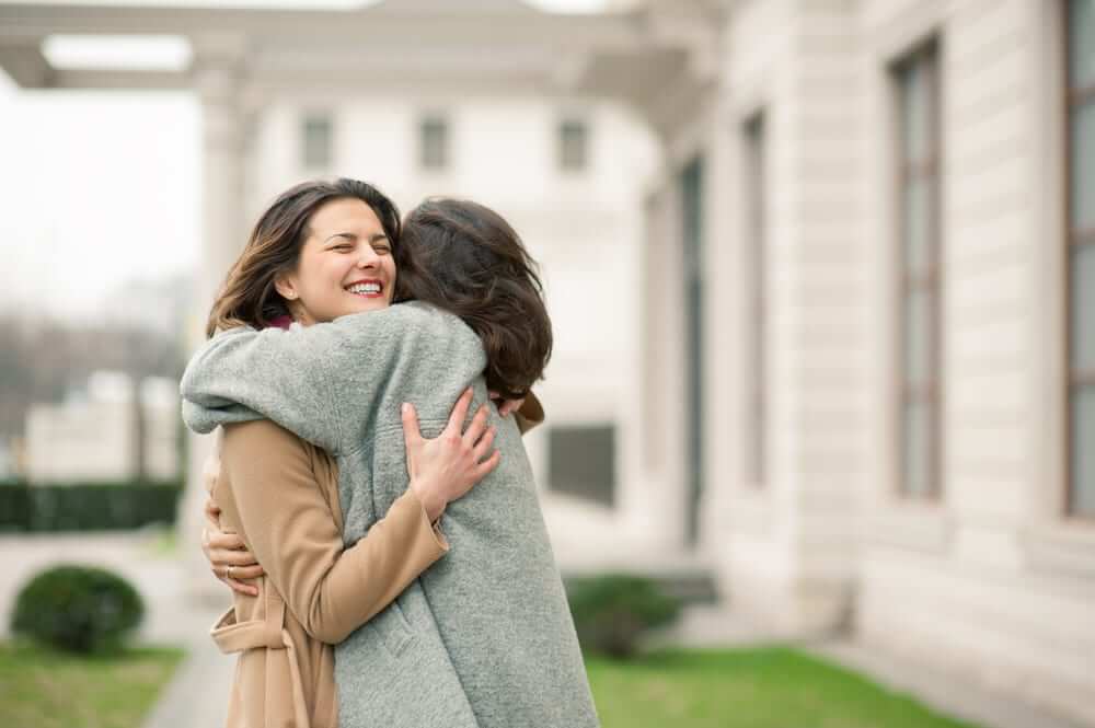 Two girls hug on the sidewalk.